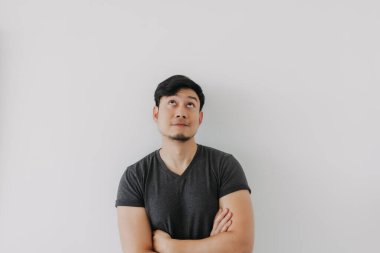 Siyah tişörtlü Asyalı adam beyaz duvarda kollarını çaprazlıyor..