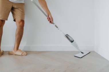 Erkek bacağı, el ele tutuşmak ve oturma odasının zeminini temizlemek için paspas kullanmak, ev işleri, ev işi kavramı. yaşam tarzı rutin kavramı.