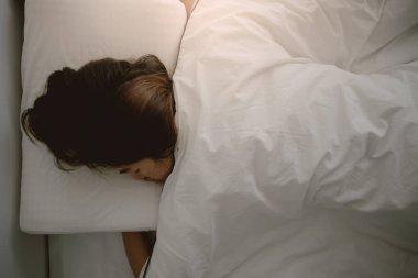 Asyalı Taylandlı bir kadının beyaz yatakta güzel rüyalar görmesi, battaniye örtüsü, odada yalnız başına dinlenmesi.. 