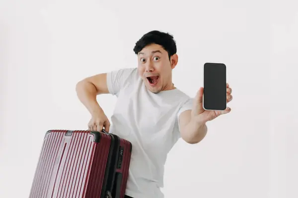 stock image Wow face Asian man holds up a suitcase and a cell phone. He seems to be ready to travel with his mobile application.