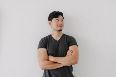 Siyah tişörtlü Asyalı adam beyaz duvarda kollarını çaprazlıyor..