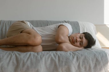 Yalnız ve depresif Asyalı bir adam dairesinde tek başına kanepede kıvrılıyor..