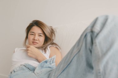 Asyalı kadın kanepede uzanıyor, saçlarıyla oynuyor ve rahatlıyor..