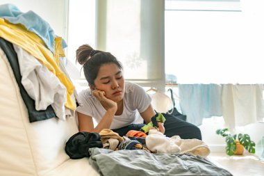 Sıkıcı yüzlü Asyalı kadın giysileri alıyor ve düzenliyor, ev işi kavramı..