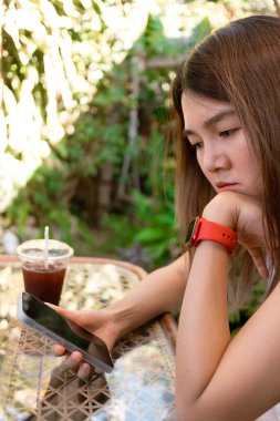 Asyalı kadının cep telefonuyla sosyal medyayı karıştırırken çekilmiş dikey fotoğrafı, üzgün ve depresif.