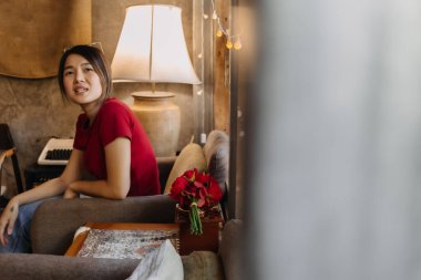 Kırmızılı Asyalı kadın rahat bir şekilde oturma odasında oturuyor..