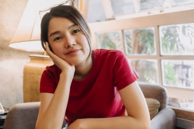 Kırmızılı Asyalı kadın rahat bir şekilde oturma odasında oturuyor..