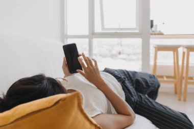 Asyalı kadın cep telefonu kullanıyor ve rahatlıyor. Otur ve kanepeye uzan. .