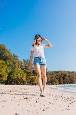 Neşeli Asyalı kadın sahilde yürüyor ve gökyüzü açık.