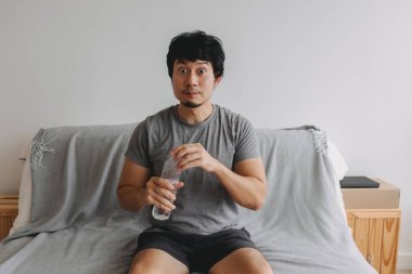 Asyalı adam odadaki kanepede oturan plastik su şişesini açıyor..