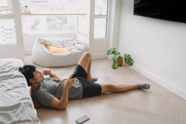 Asyalı bir adam haftasonu oturma odasında uzanıp film izliyor..