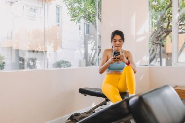 Sarı Mavili formalı tembel Asyalı kadın spor salonunda cep telefonu kullanıyor..