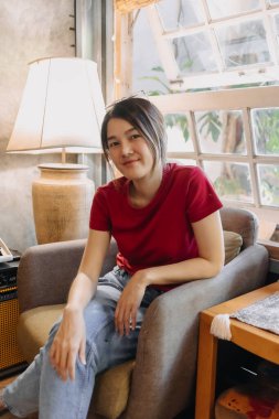 Kırmızılı Asyalı kadın rahat bir şekilde oturma odasında oturuyor..