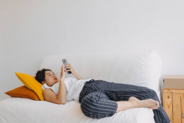 Asyalı kadın cep telefonu kullanıyor ve rahatlıyor. Otur ve kanepeye uzan. .