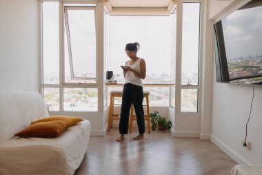 Asyalı bir kadın odasında dolanıp cep telefonuyla sohbet ediyor..