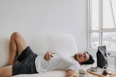 Asyalı adam kahvesini bitirdikten sonra kanepede kestiriyor..