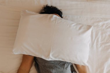Uykucu Asyalı adam yüzünü yastıkla örterek yatağında uyumaya devam ediyor..