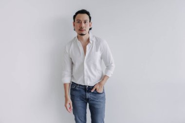 Dalgın yüzlü, uzun saçlı, beyaz gömlekli, beyaz kot pantolonlu Asyalı adam..