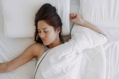 Beyaz yatakta uyuyan Asyalı kadın, geç kalkıyor..