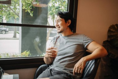 Mutlu Asyalı adam kafede rahatlamış, buzlu kahve içiyor..