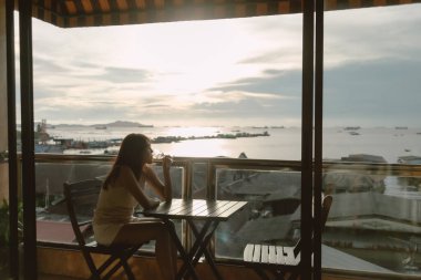 Bekar bir kadın tek başına içiyor, Asya deniz köyünün günbatımının tadını çıkarıyor..