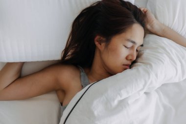 Beyaz yatakta uyuyan Asyalı kadın, geç kalkıyor..