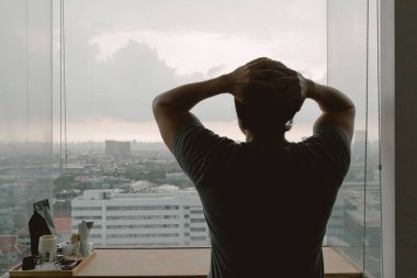 Yalnız, bekar Asyalı bir adam apartmanın penceresinden dışarı bakıyor..