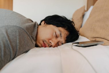 Uykucu Asyalı adamın yüzünü kapat. Cep telefonu kafasının yanında kalmış.