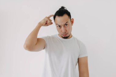 Tereddüt etme komik yüzlü beyaz tişörtlü Asyalı adam beyazları soyutluyor..