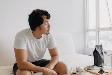 Boş kafalı Asyalı adam elinde kahve fincanıyla pencereden dışarı bakıyor..