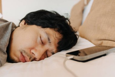 Uykucu Asyalı adamın yüzünü kapat. Cep telefonu kafasının yanında kalmış.