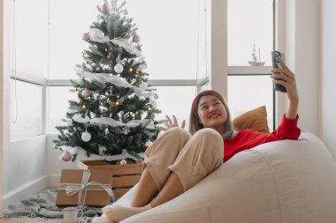 Mutlu kırmızı tişörtlü Asyalı kadın Noel ağacını gösteren arkadaşları ve ailesiyle kutlama için video görüşmesi yapıyor. - Evet. Yüksek kalite fotoğraf