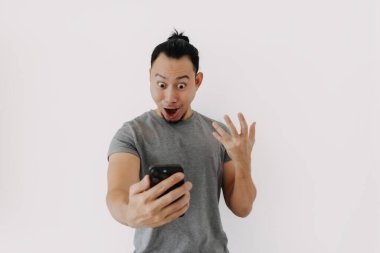 Gri tişörtlü Asyalı adam beyaz üzerinde akıllı telefon uygulaması kullanıyor..