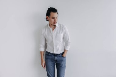 Dalgın yüzlü, uzun saçlı, beyaz gömlekli, beyaz kot pantolonlu Asyalı adam..