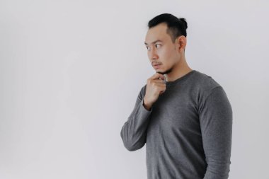 Gri yün katmanlı Asyalı adamın beyazın üzerinde durduğunu düşünüyor..