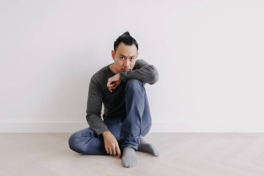 Yalnız, bağımsız, yaratıcı Asyalı adam boş beyaz odada tek başına oturuyor..