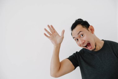 Neşeli Asyalı adam siyah tişörtle selam vermek için el sallıyor..