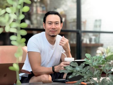 Kafedeki tablet bilgisayarında çalışan mutlu Asyalı adam..