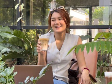 Mutlu bir gülümseme. Asyalı kadın kafede çalışırken buzlu kakao içiyor..