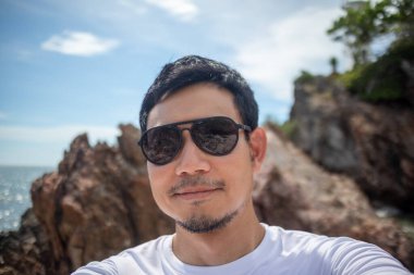 Genç erkek, arka planda deniz ve kayalık kıyılarla kendi portresi için poz veriyor.