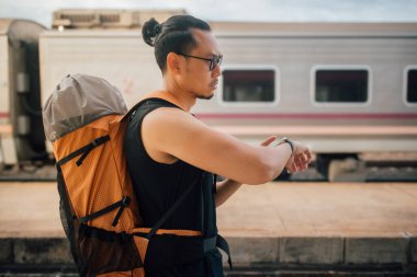 Asyalı turist sırt çantalı. Saate bak. Treni bekle..