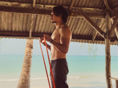 Deniz kenarındaki kulübede lastik bant ile egzersiz ve egzersiz. Asya 'da plaj rahatlığı..