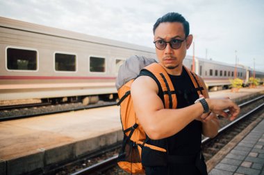 Asyalı turist sırt çantalı. Saate bak. Treni bekle..