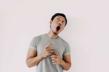 Genç Asyalı erkek dramatik bir duruş ve geniş gözlerle inançsızlığını ifade ediyor.