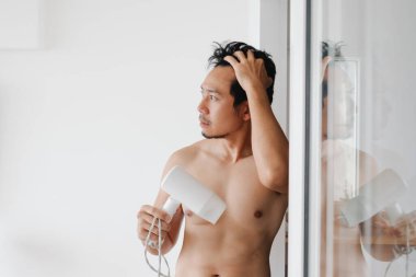 Asyalı erkek parlak, temiz, modern yatak odasında cam aynanın yanında tımarlanıyor.