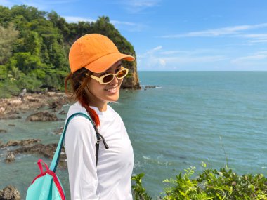 Turist tropikal ortamda açık mavi gökyüzü altında kıyı manzarasının tadını çıkarıyor