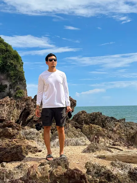 Gezgin, güpegündüz tropikal kayalık sahilde manzaranın tadını çıkarıyor.