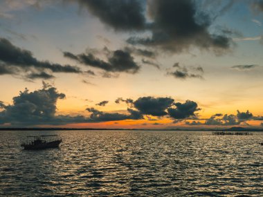 Gün batımında sakin denizde yüzen tekneli renkli bir akşam göğü.