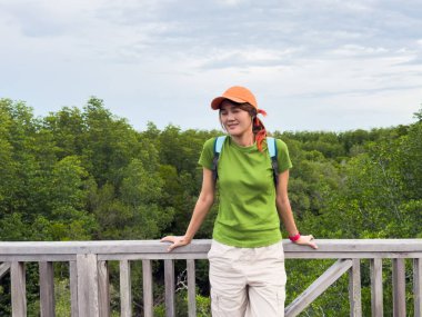 Etrafı yeşilliklerle çevrili ahşap bir yolda doğaya hayran olan kadın gezginin yan görüntüsü