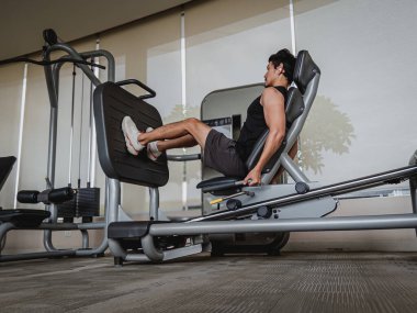 Taylandlı erkek, kaslı bacakları var. Bacak pres makinesi üzerinde egzersiz yapıyor. Kapalı modern spor salonunda vücut egzersizi yapıyor.
